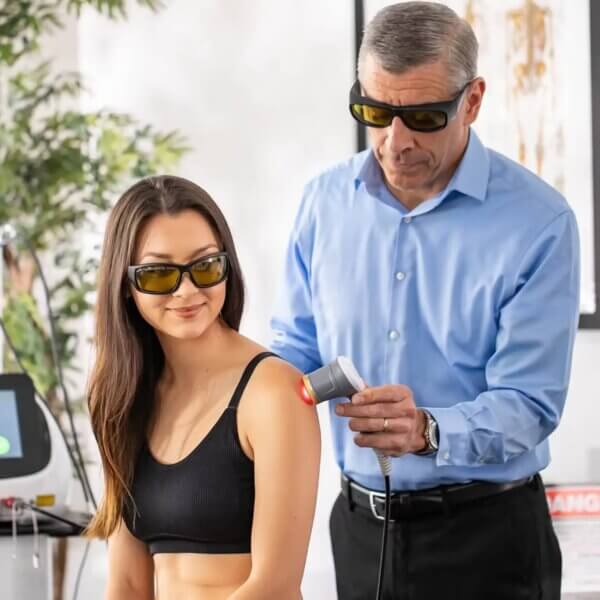 Healthcare provider administering laser therapy vs traditional pain relief to shoulder of woman