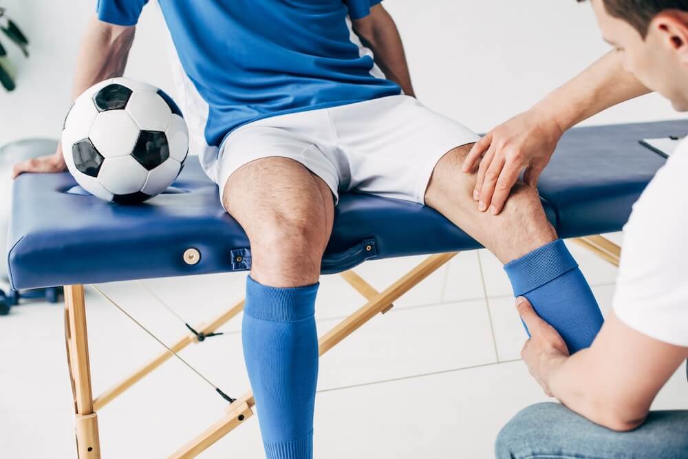 Athlete holding soccer ball on a table getting his knee looked it with light therapy in sports medicince